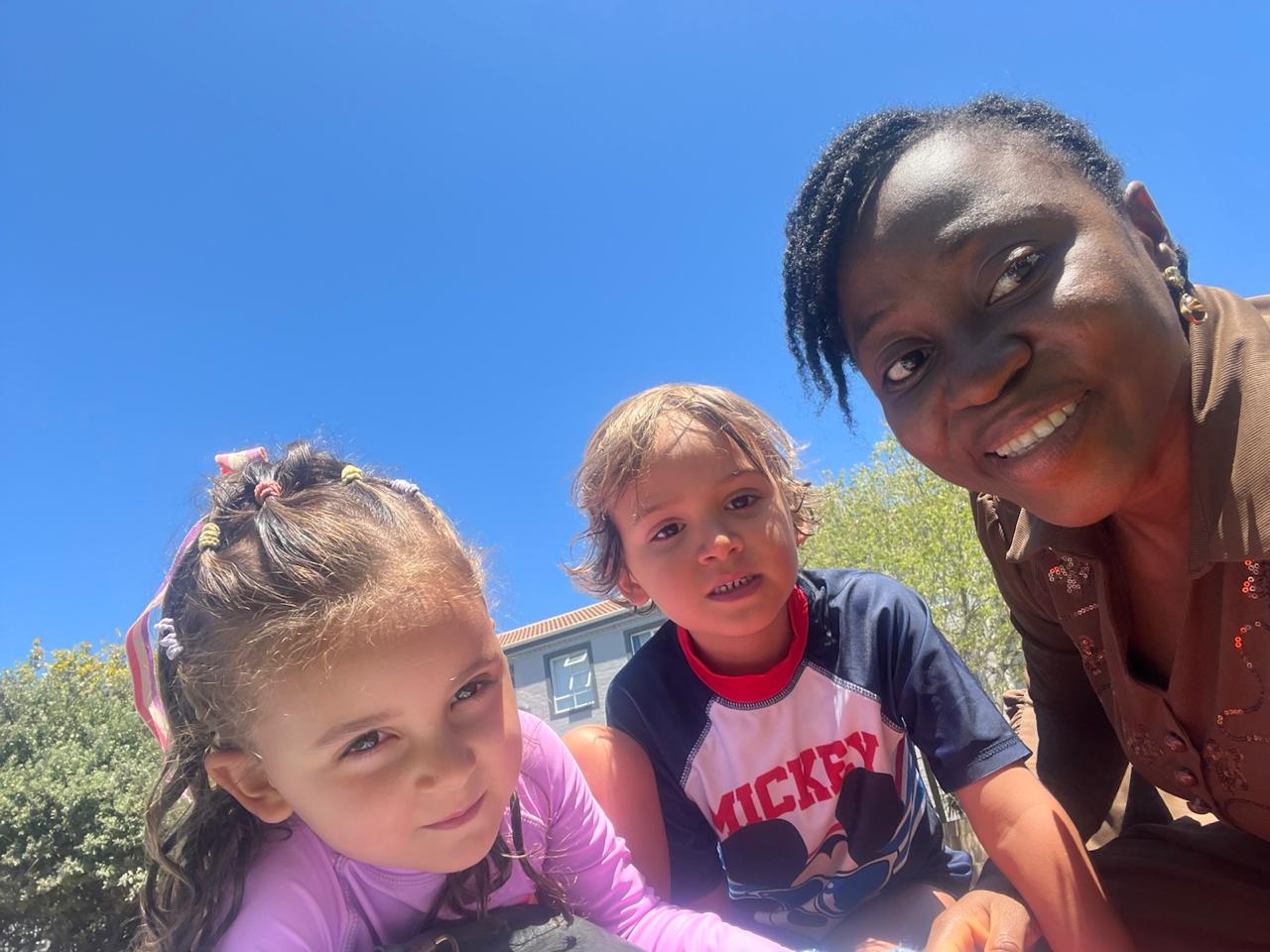 Grace Damilola with two children smiling at the camera on a sunny lawn