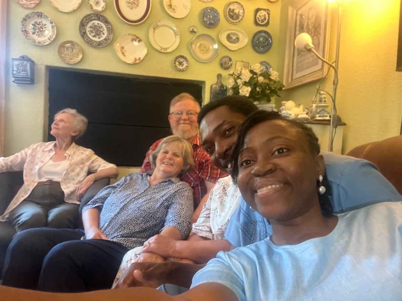 Grace Damilola taking a selfie with brothers and sisters on the couch beneath a wall of decorative plates