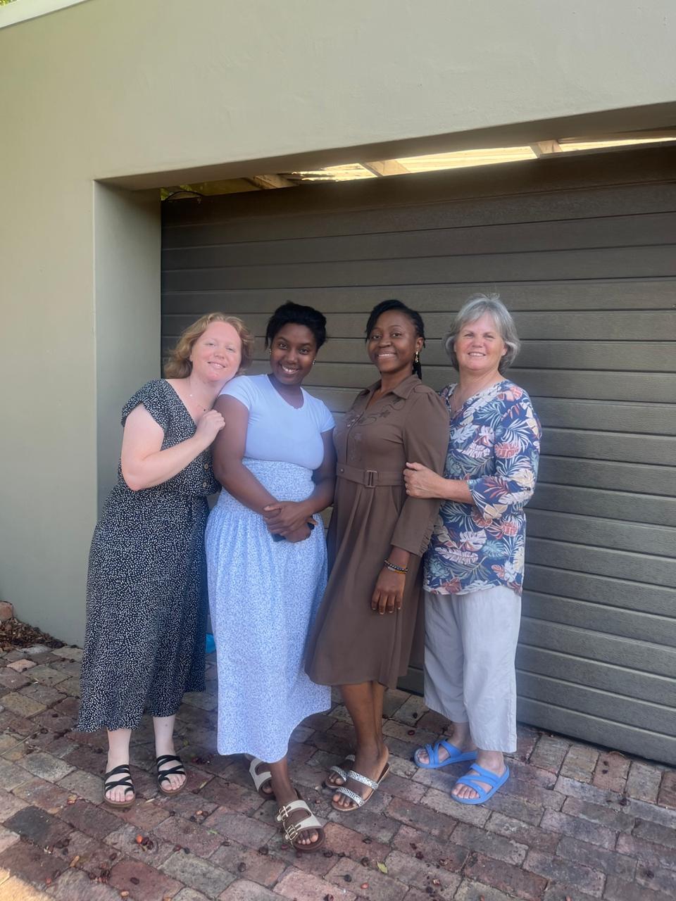 Four sisters standing arm in arm and smiling in front of a garage door