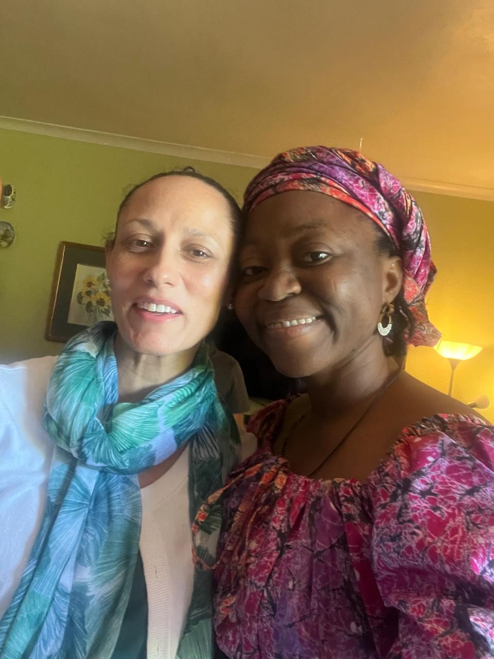 Grace Damilola in a floral headwrap taking a selfie with a smiling sister