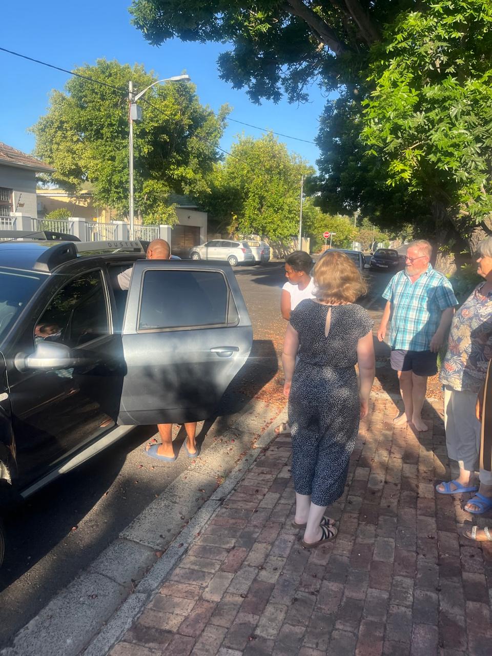 John being welcomed by brothers and sisters as he arrives by car on a sunny Cape Town street