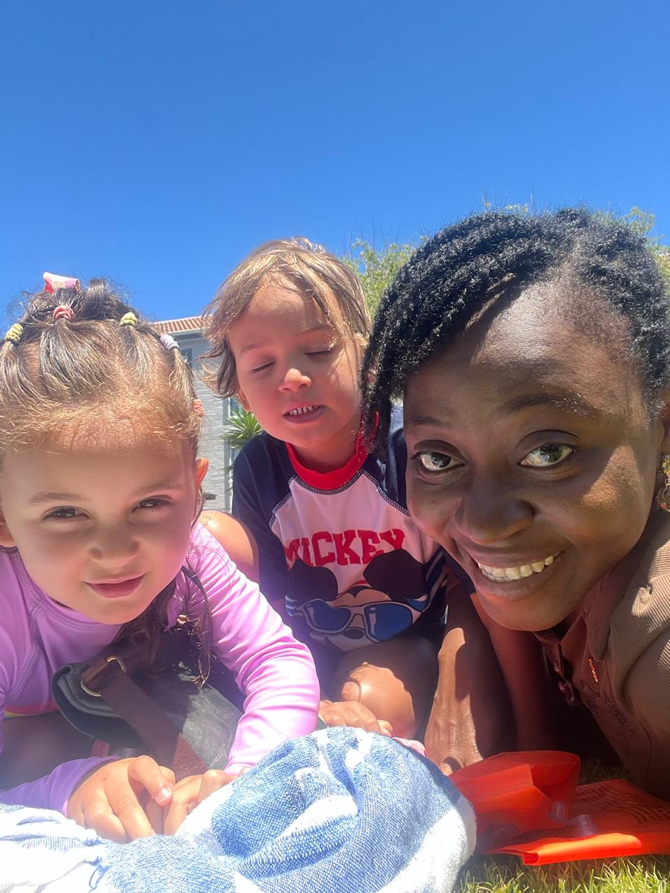Grace Damilola lying on the grass in the sunshine with two smiling children