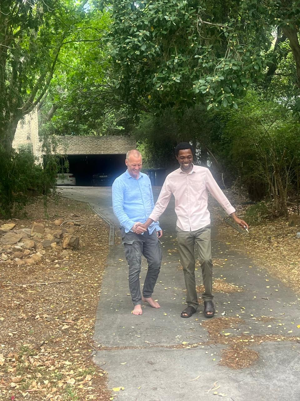 John Damilola laughing and shaking hands with a brother on a tree-lined driveway